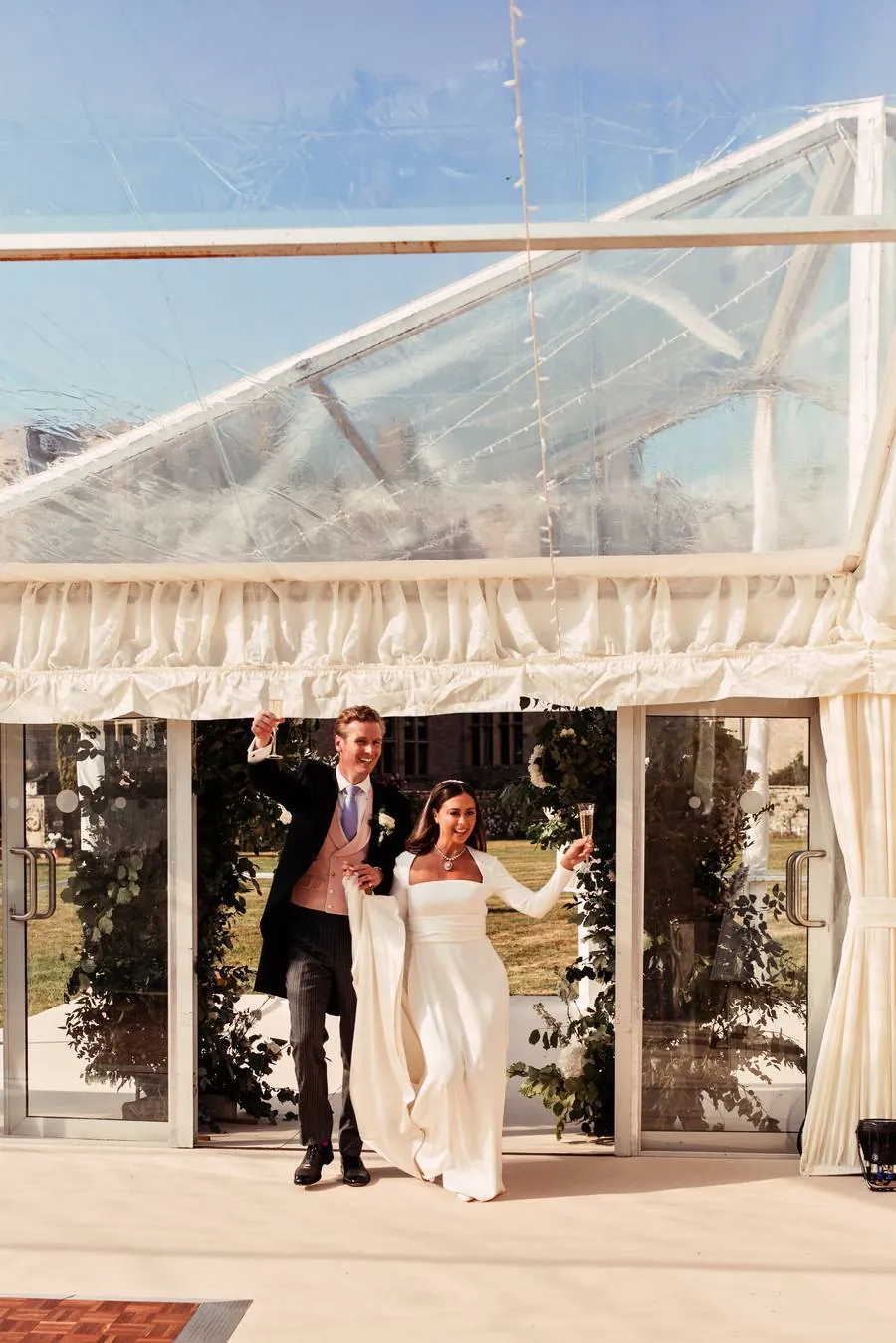 Bride and groom raising their glasses as they step into the marquee