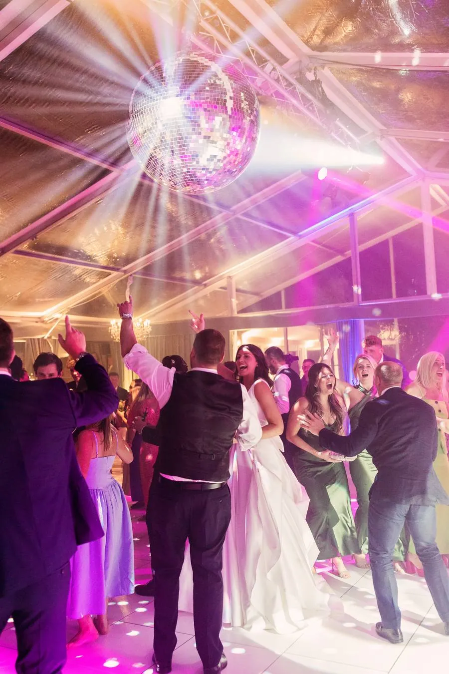 Bride and guests dancing beneath a mirror ball with pink lighting