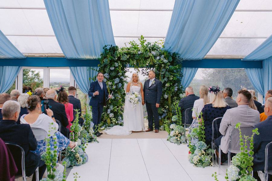 Ceremony under a floral arch in a marquee with pale blue drapes