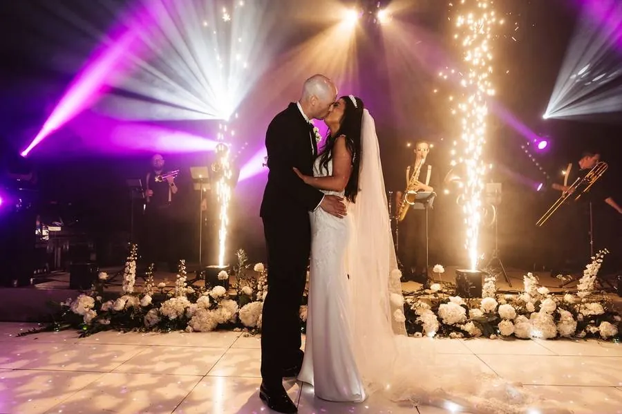 Couple sharing a first dance kiss with sparkler fountains, stage lighting and a live band behind them