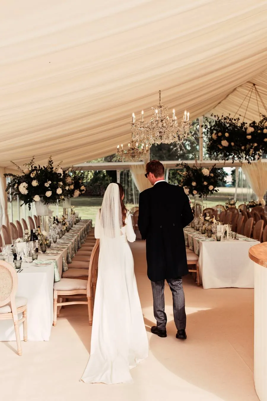 Couple walking into the marquee past long tables and flowers