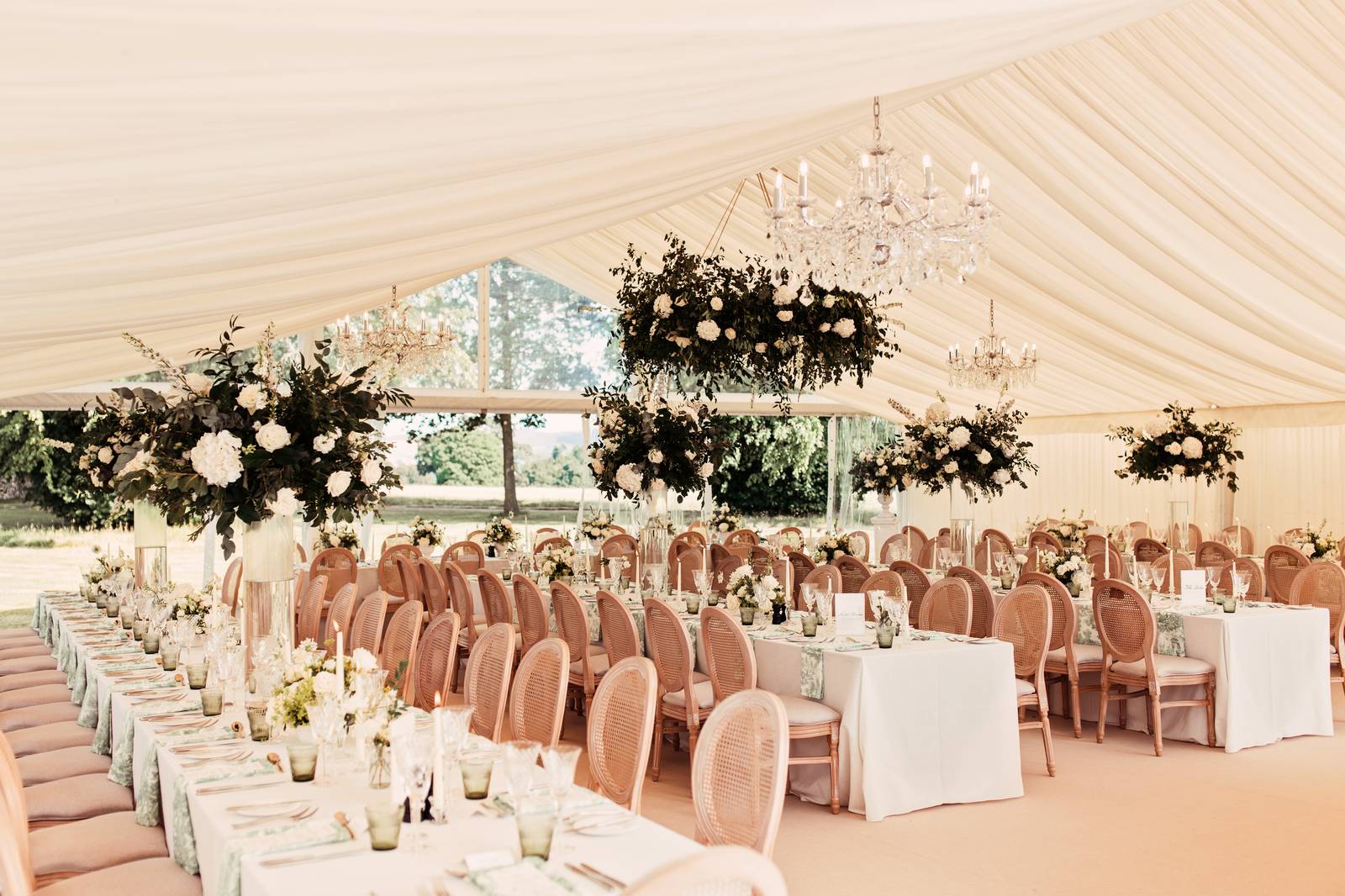 Cream-lined marquee with long tables, hanging flowers and chandeliers