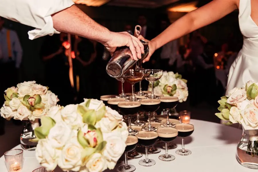 Espresso martini tower being poured, with white roses and orchids in the foreground