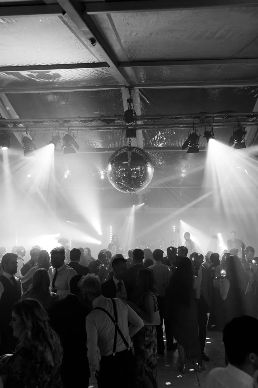 Guests dancing beneath a mirror ball and stage lighting, in black and white