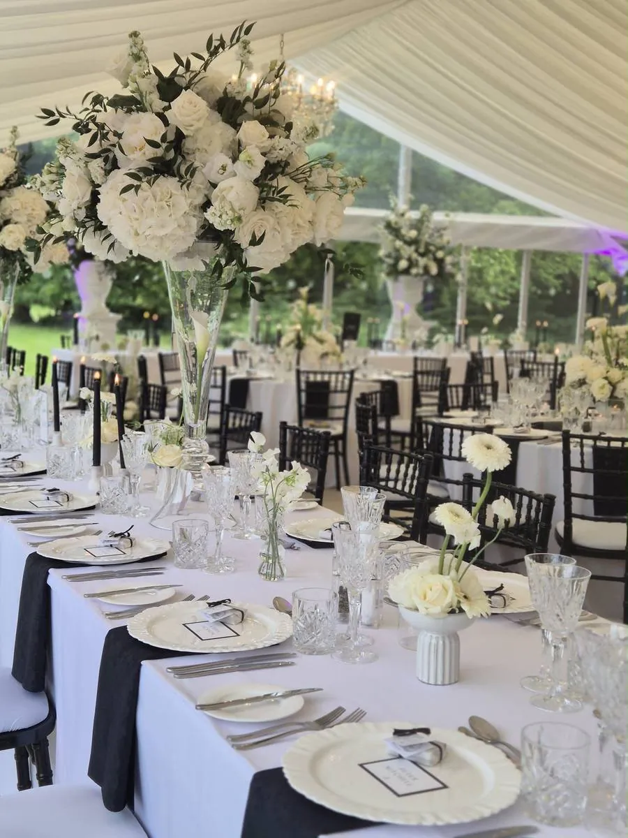 Long table with black napkins, crystal glassware and tall white flower arrangements