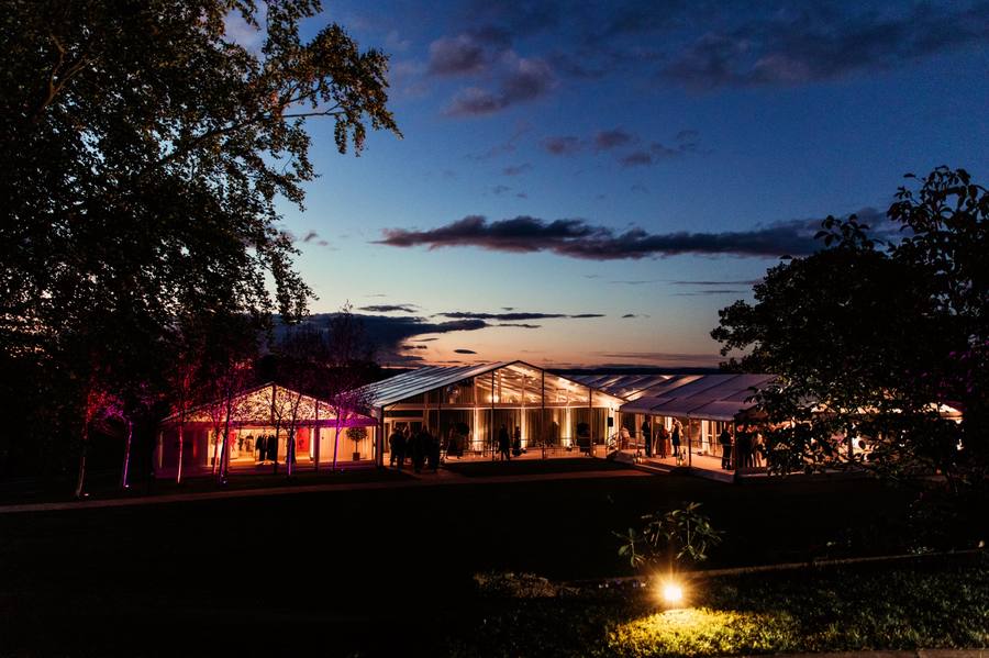 Marquee glowing at dusk under a deep blue sky, with guests on the terrace