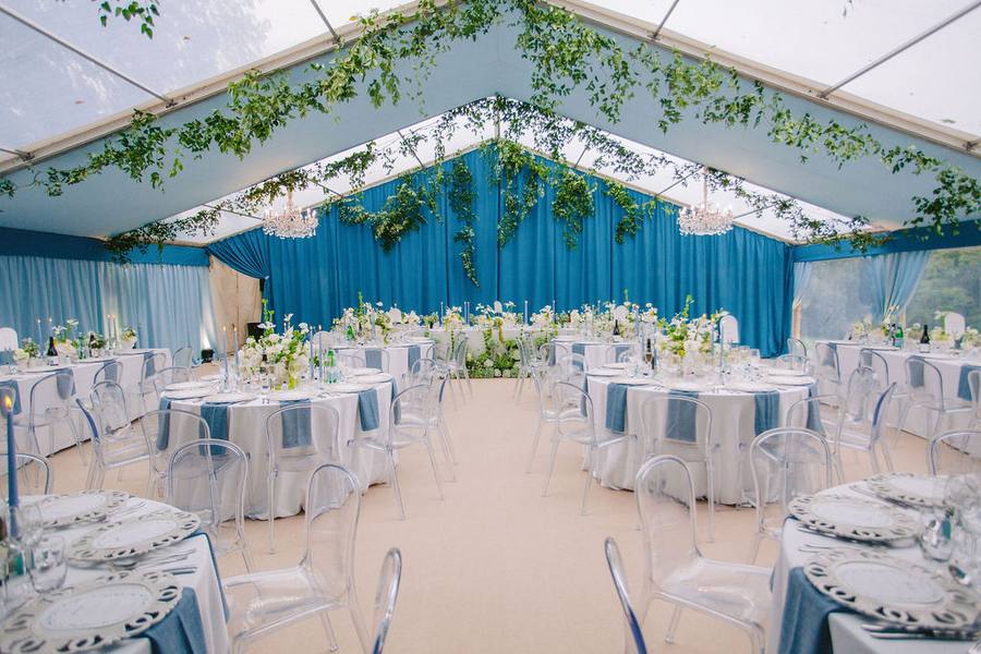 Marquee interior with round tables, blue drapes and hanging greenery