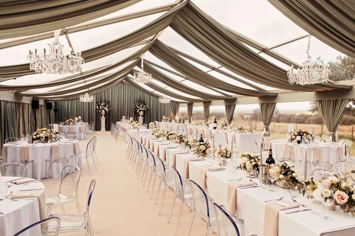 Marquee set for a wedding breakfast with sage draping, chandeliers and long tables