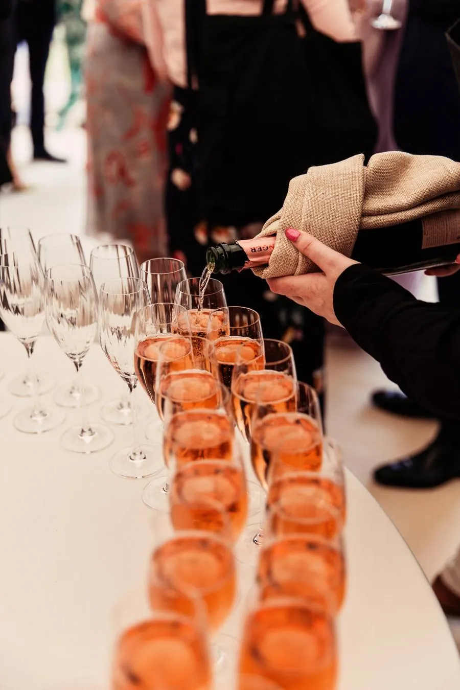 Rosé champagne being poured into a row of glasses on a round table
