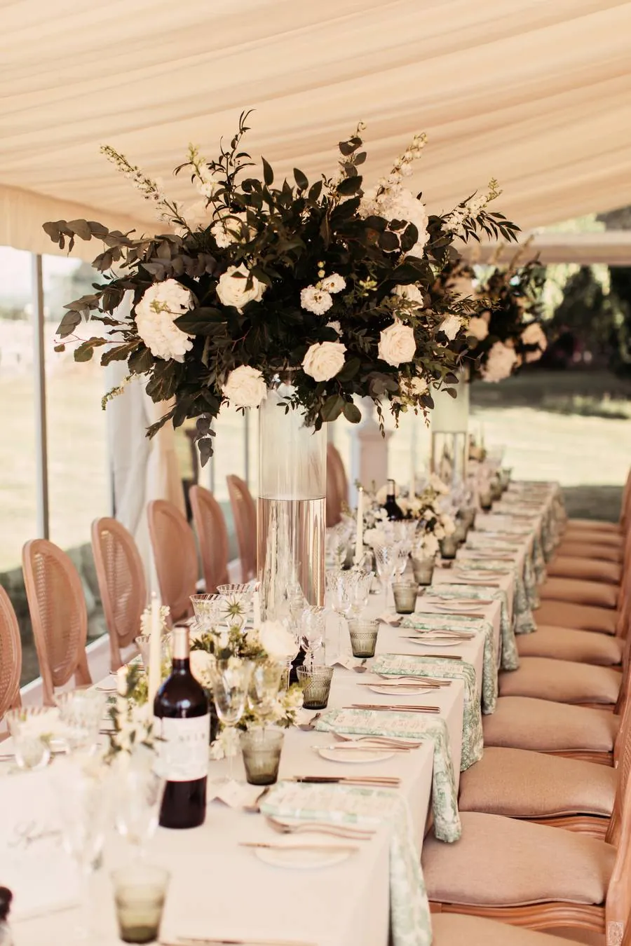 Tall floral arrangement on a long table with rattan chairs