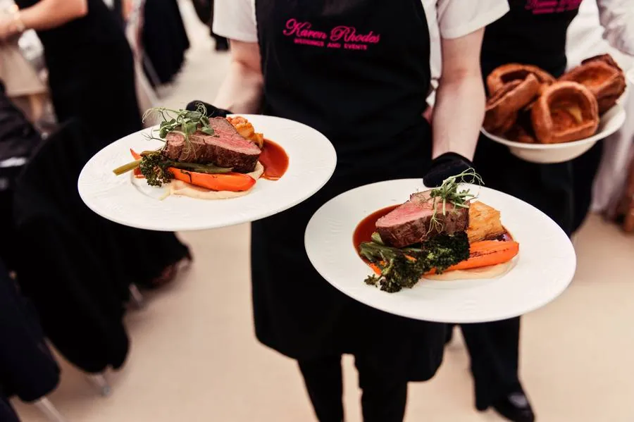 Waiting staff carrying plates of beef fillet, with a bowl of Yorkshire puddings